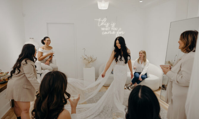 bride standing in the middle of room showing wedding dress to group of friends