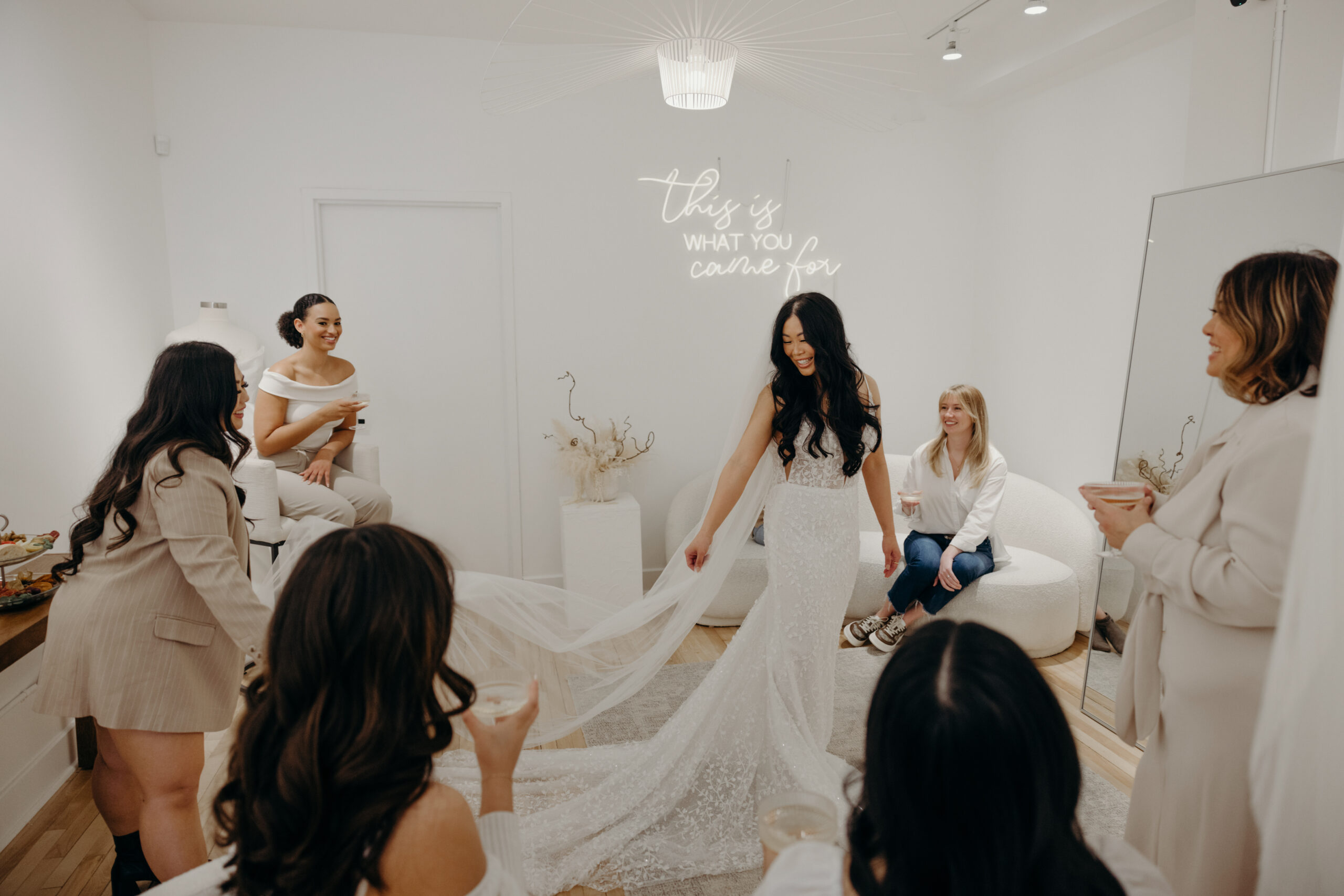 bride standing in the middle of room showing wedding dress to group of friends